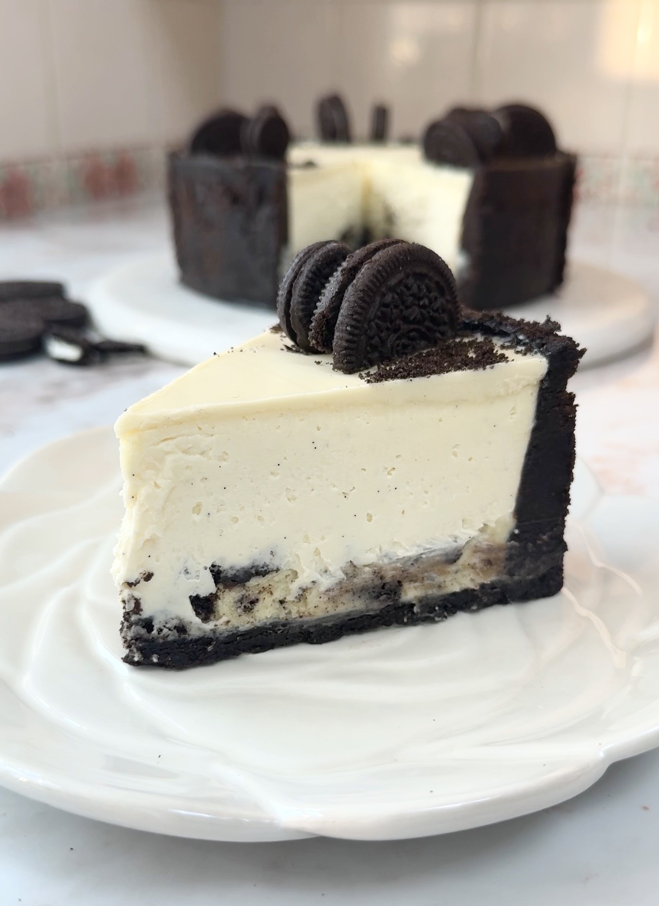 Creamy no bake Oreo cheesecake slice topped with melted white chocolate and crushed Oreo cookies