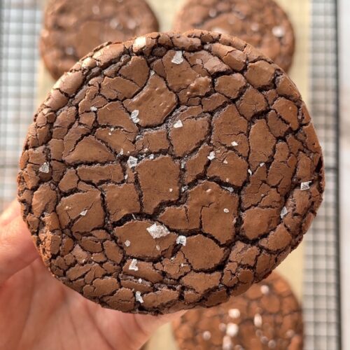 Shiny crackly brownie cookies with fudgy centres and flaky sea salt on a baking tray